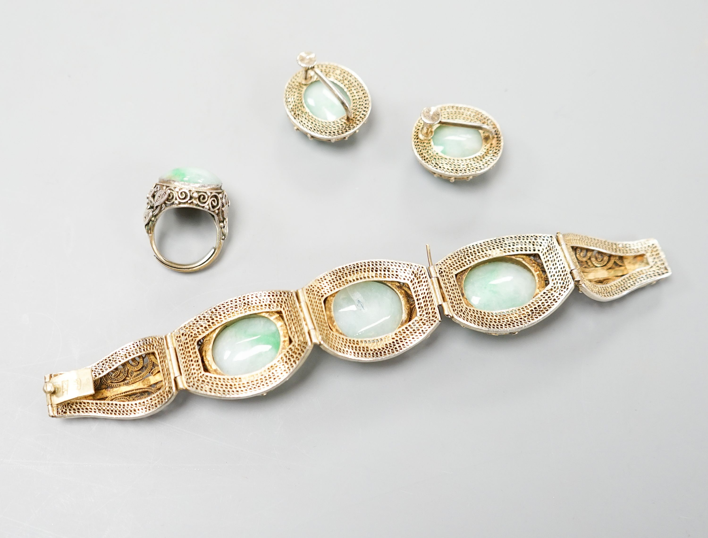 A Chinese filigree gilt white metal and three stone cabochon jade set bracelet, 17cm, a pair of matching ear clips, length 25mm and a similar white metal and cabochon jade set ring, size L.